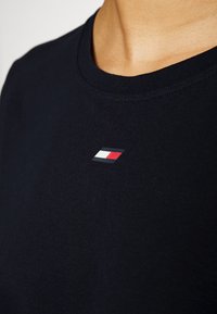 Námořnická modrá bavlněná tričko s kulatým výstřihem. Na hrudi má malé logo v červené, bílé a modré barvě. Hladká textura.