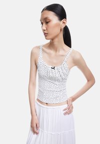 Hvid tanktop med prikker, der har en samling i sømmen og en sort sløjfe ved halsudskæringen, parret med en svævende hvid nederdel.