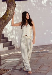 Ensemble en lin rayé composé d'un gilet sans manches avec boutons et d'un pantalon ample. Couleurs claires avec des rayures verticales et une texture détendue.