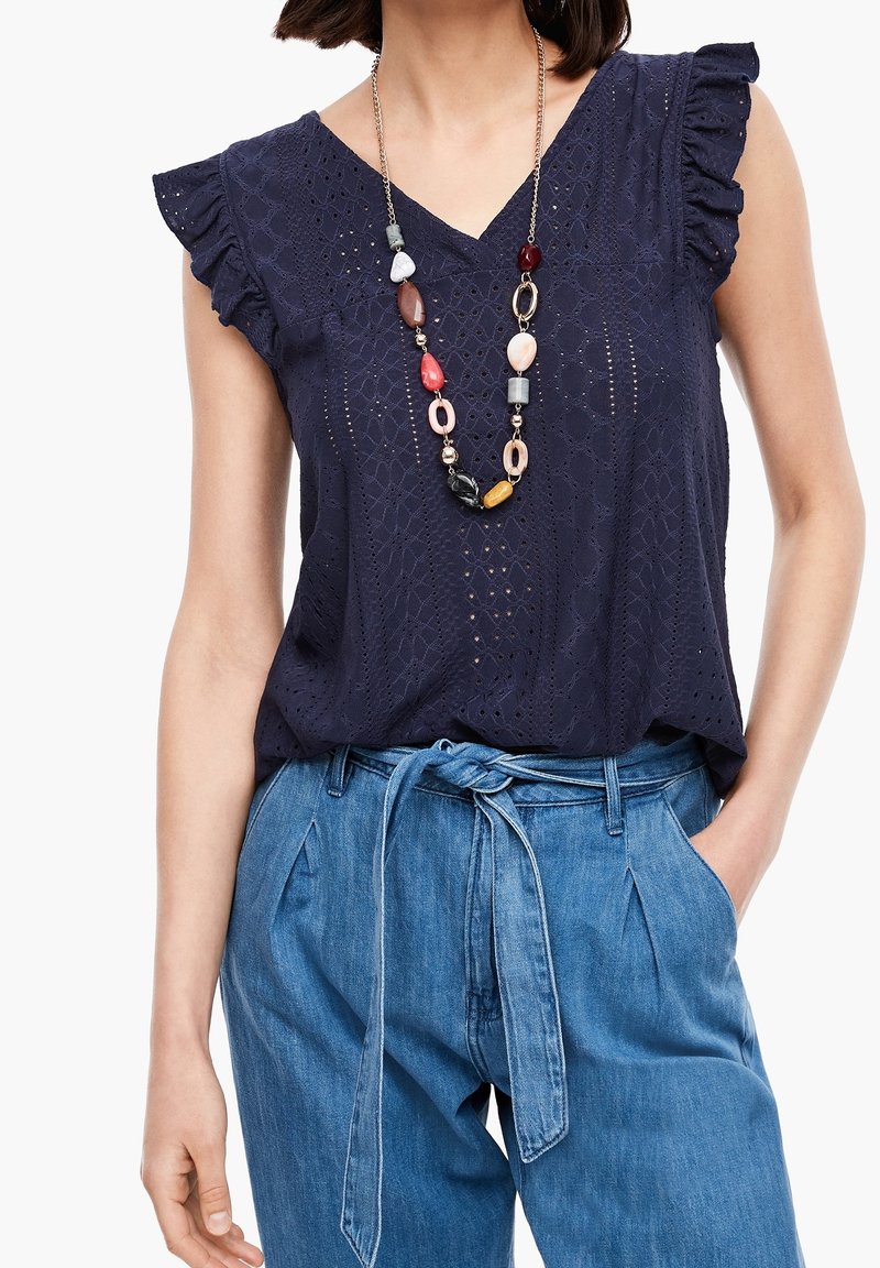 Haut bleu marine à œillets avec manches à volants, associé à un pantalon taille haute bleu clair et un collier de perles multicolores.