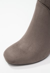 Gros plan sur la partie avant du pied d'une bottine en daim taupe sur fond blanc.