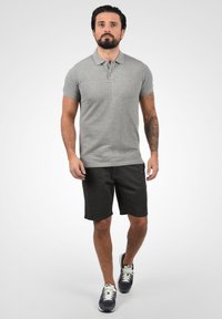 Grå polo-skjorte med krage, kort ermer, kombinert med svarte shortser. Uformell tekstur med en tettsittende design. Hvite og marineblå sneakers.