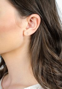 Orecchini a perno in argento a forma di sole con raggi appuntiti, posti su uno sfondo neutro, indossati in un orecchio forato.