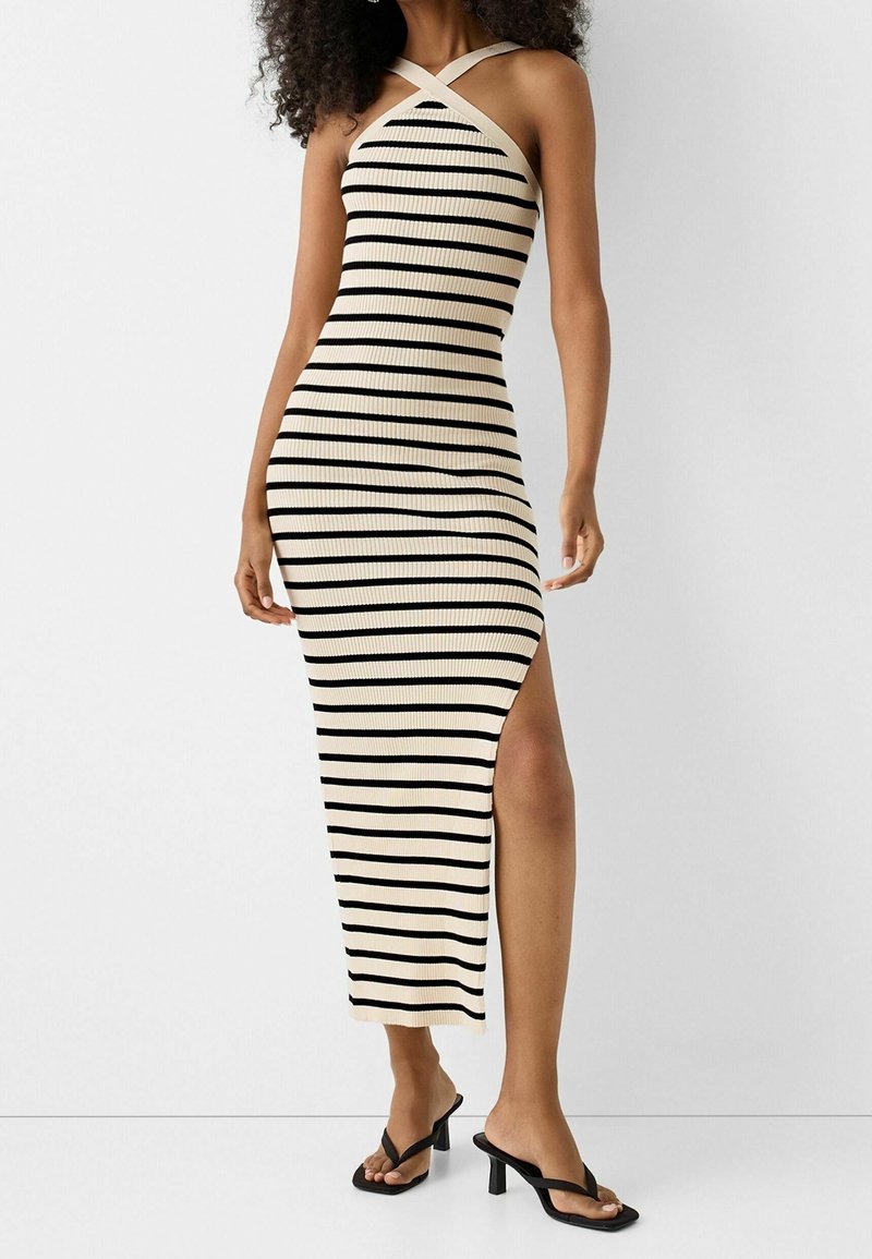 Robe midi côtelée à rayures horizontales noires et crème, avec un design à bretelles croisées et une fente latérale haute sur la cuisse.
