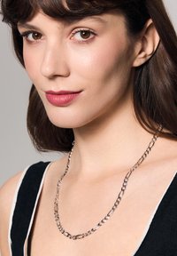 Srebrny naszyjnik łańcuszkowy z przeplatającymi się owalnymi i okrągłymi ogniwami, o gładkiej teksturze i wypolerowanym wykończeniu. Noszony na szyi.