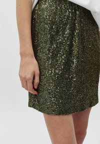 Gonna verde in paillettes con un design aderente, caratterizzata da una texture scintillante, un'orlo sopra il ginocchio e un effetto luccicante sottile.