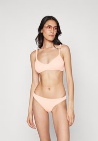 Ensemble de bikini côtelé pêche comprenant un haut triangle à fines bretelles et des culottes taille basse assorties. Texture lisse, design minimaliste.