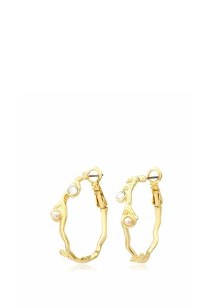 Boucles d'oreilles en forme d'anneaux dorés avec un design torsadé irrégulier, chacune ornée d'une petite perle et d’un accent en pierre précieuse claire près du fermoir.