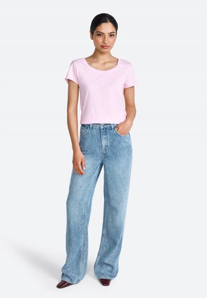 T-shirt rose clair à manches courtes associé à un jean large taille haute bleu clair. Tissu lisse et coupe classique. Chaussures à talons brunes.