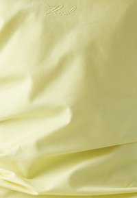 Tissu jaune avec une texture lisse, présentant un léger relief et un "Karl" brodé dans le coin supérieur gauche.