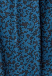 Tissu bleu avec un motif abstrait noir irrégulier, montrant des plis et une surface texturée.