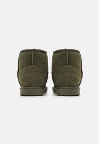 Bottines en daim vert avec une texture douce, une forme arrondie et des coutures renforcées à l'arrière, équipées d'une semelle en caoutchouc légèrement surélevée.