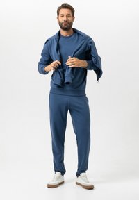 Blauw katoenen sweatshirt en joggingbroek, met geribde boorden en tailleband. Witte sneakers met bruine accenten maken de outfit compleet.