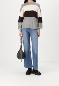 Sweter z dzianiny w szare, kość słoniową i ciemnobrązowe poziome paski; zestawiony z niebieskimi szerokimi spodniami i czarnymi masywnymi butami. Akcesoria to ciemnoszara torba.