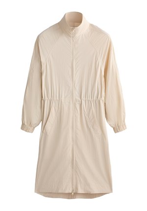Veste beige clair à manches longues avec un col haut, fermeture éclair à l'avant, poignets élastiques et taille ajustable. Comprend deux poches latérales.