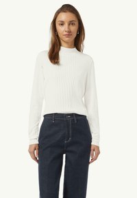 White ribbed sweater with a high neckline and vertical texture details, paired with dark blue high-waisted denim pants featuring contrasting stitching.