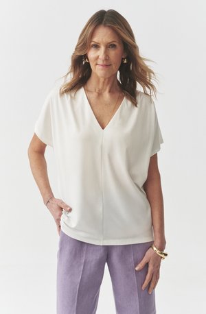 White loose-fitting blouse with a V-neck, short sleeves, and smooth texture, paired with light purple linen pants.