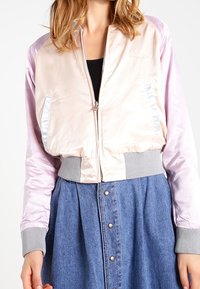 Lekka kurtka bombowca z satynowym różowym korpusem, błyszczącymi fioletowymi rękawami, prążkowanymi szarymi mankietami i ściągaczem, z zamkiem błyskawicznym z przodu.