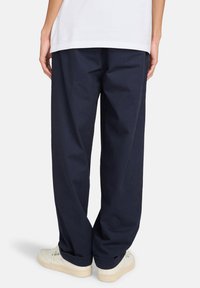 Navy blue cotton trousers with a loose fit, featuring a straight leg, single back pocket, and subtle stitching details.