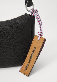 Sac en cuir texturé noir avec fermeture éclair. Il est doté d'une sangle tressée colorée et d'une étiquette marron portant la mention "KARL LAGERFELD."