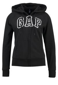 Svart zip-up huvtröja med framfickor och en stor vit "GAP"-logotyp. Har en justerbar huva och ribbad mudd för en tight passform.