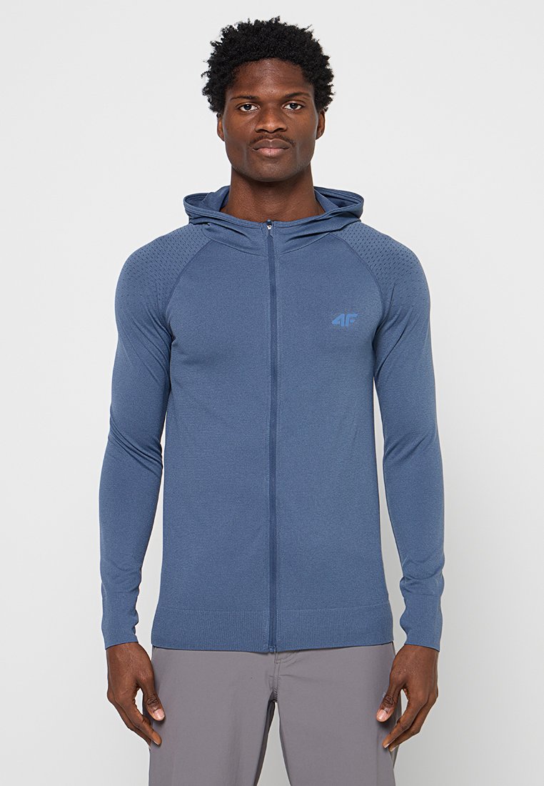 Niebieska bluza z długim rękawem, zapinana na zamek, wykonana z teksturowanego materiału, z kapturem i ściągaczami na rękawach. Posiada małe logo na lewej piersi.