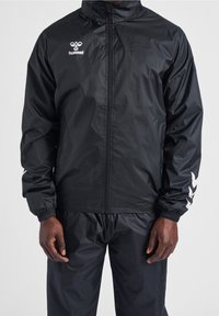 Giacca leggera nera con chiusura a zip, polsini elasticizzati e logo bianco sul petto. Presenta strisce bianche a contrasto sulle maniche.