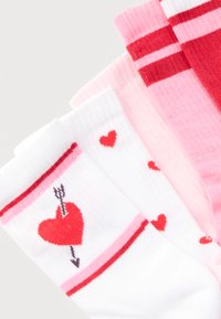 Τέσσερα ζευγάρια πολύχρωμων καλτσών με μοτίβα καρδιών και βελών, που περιλαμβάνουν ρίγες και μονόχρωμο ροζ, διατεταγμένα επικαλυπτόμενα σε λευκό φόντο.