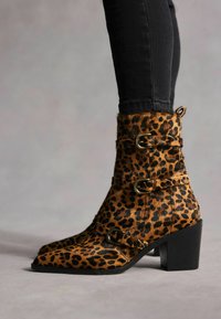 Čizme do gležnja s uzorkom leoparda napravljene od umjetnog krzna, sa tri kopče, šiljastim vrhom i debelim petama. Crni naglasci upotpunjuju dizajn.