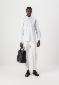 Cămașă butonată de culoare albastru deschis, cu buzunar pe piept și logo galben, asociată cu pantaloni albi și mocasini negri. Geantă de umăr neagră cu două mânere.