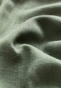 Tissu vert texturé avec un tissage doux, affichant de subtiles variations de profondeur et de lumière, créant une apparence naturelle et organique.