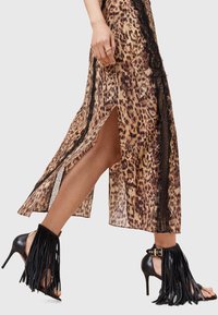 Abito a stampa leopardo con accenti in pizzo nero, caratterizzato da uno spacco alto fino alla coscia e abbinato a sandali neri con tacco alto e dettagli in frange.
