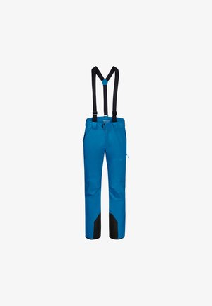 Homme portant un pantalon de ski bleu, des chaussures de ski rouges, un haut noir et des bretelles, tenant des bâtons de ski rouges et noirs en marchant.