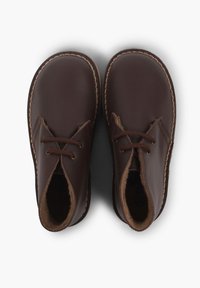 Hnědé kožené boty s kulatou špičkou, šněrovacím designem a šitými okraji. Měkká vnitřní podšívka pro pohodlí.