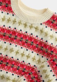 Jersey de punto con base blanca y vibrantes rayas rojas y negras, acentos metálicos dorados y un escote de canalé. Detalle de patrón texturizado.