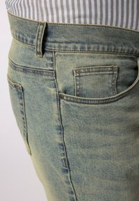 Jeans de mezclilla azul claro con un acabado desgastado, diseño de cinco bolsillos, acentos de costura visibles y un detalle de un solo bolsillo trasero.