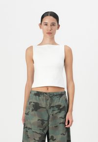 Valge lühike tank top ruudukujulise kaelusega, koos vabalt langevate kamuflaažimustriga pükstega. Sile tekstuur, minimaalne disain.