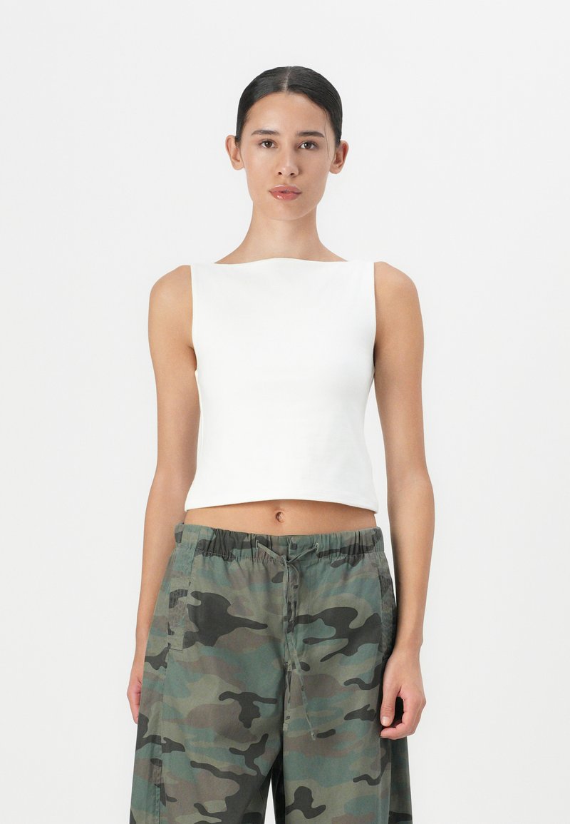 Valge lühike tank top ruudukujulise kaelusega, koos vabalt langevate kamuflaažimustriga pükstega. Sile tekstuur, minimaalne disain.