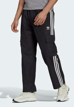 Pantaloni cargo neri con logo bianco Adidas e tre strisce verticali. Caratterizzati da tasche laterali e una vestibilità rilassata. Realizzati in un tessuto resistente.
