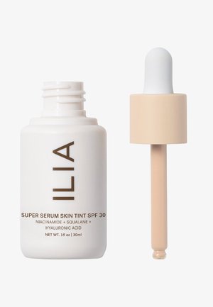 ILIA Super Serum Skin Tint SPF 30 in un flacone bianco con testo marrone, dotato di un contagocce beige per erogare il liquido. Capacità di 30 ml.