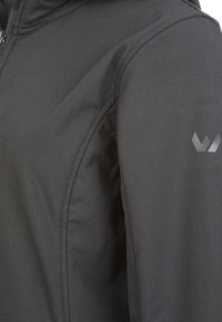 Musta takki, jossa on sileä, matta kangas, vetoketjukiinnitys, kulmikkaat saumat ja hienovarainen logon yksityiskohta hihassa.