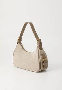 Bežinė zomšinė petneša su kreiviu formatu, kontrastinga ruda odinė juostele ir auksinės spalvos aksesuarais. Užtrauktukas viršuje.