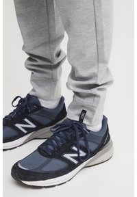 Navy blue athletic shoes with grey accents and white logo, paired with light grey, textured pants. Shoes feature laces and visible soles.