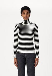 Maglione a collo alto a righe in tessuto a coste bianco e nero, con maniche lunghe e un design aderente, abbinato a jeans scuri.