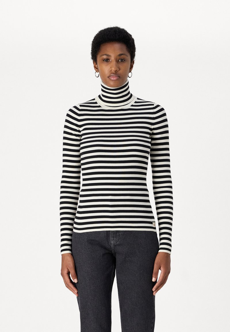 Maglione a collo alto a righe in tessuto a coste bianco e nero, con maniche lunghe e un design aderente, abbinato a jeans scuri.