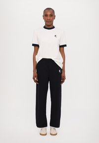White T-shirt with navy ribbed collar and cuffs, featuring a logo. Paired with black sweatpants with logo and white trimming at the hem.