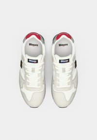 Λευκά και γκρι αθλητικά παπούτσια με σουέντ φινίρισμα, επίπεδα κορδόνια, κόκκινες λεπτομέρειες στη φτέρνα και επώνυμα εσωτερικά πέλματα σε μαύρο και μπλε χρώμα.