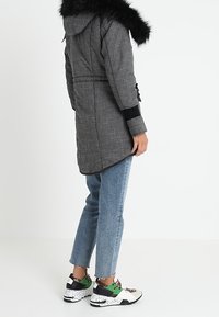 Grå rutiga parka med svart konstpäls, elastisk midja, långa ärmar och fickor, ihop med ljusblå jeans och sportiga svarta skor.