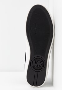 Semelle en caoutchouc noir avec une surface texturée, arborant un logo MK circulaire. Le bord est blanc, contrastant avec le noir.