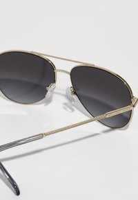 Aviator solbriller med mørke grå linser, guld metalramme, teksturerede stænger og klare næsepuder. "MICHAEL KORS" graveret på stangen.